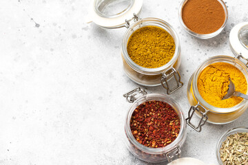 Spices and condiments in glass jars on a light gray table. Spices close-up with space for text. The view from the top