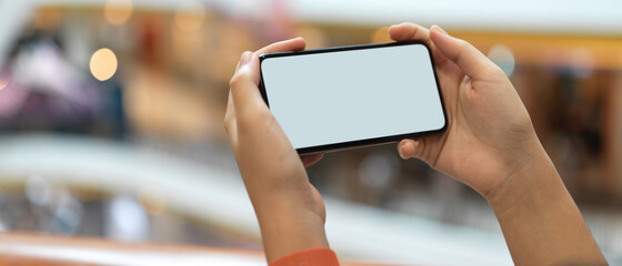 A girl holding horizontal mock-up smartphone while standing at balcony in shopping mall