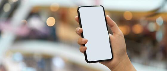 A girl holding mock-up smartphone while standing at balcony in blurred shopping mall background