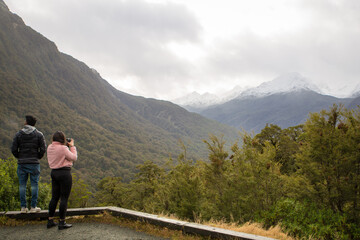 Two asian tourists take photos of the scenery at a lookout on Milford Road, Fiordland National Park, New Zealand
