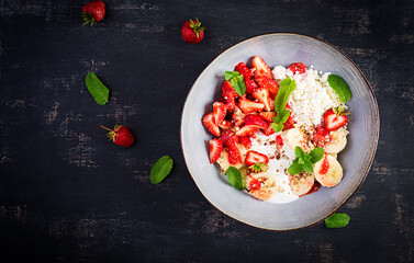 Cottage cheese or curd cheese with strawberries, bananas, walnuts in a blue bowl. Healthy food. Top view, overhead,  copy space