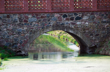 old historic stone and wood bridge over water with plant cover