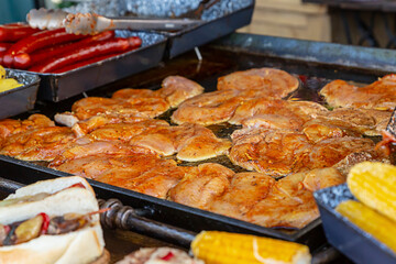 raw and seasoned chicken steak on an iron tray among sausages and corn, selective focus