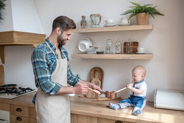 Smiling bearded man in apron getting ready the breakfast for his little son