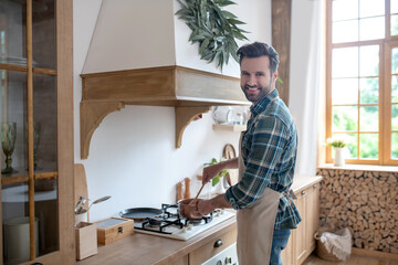 Smiling bearded man in apron standing near the oven
