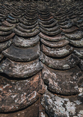 Brown and black tiles on the roof of an old house hit by wind and rain