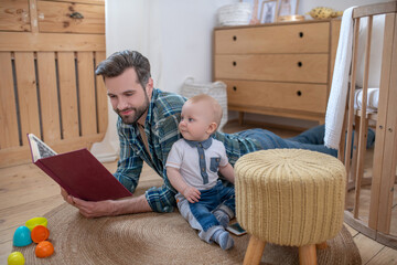 Father in a checkered shirt reading a book to his cute baby boy