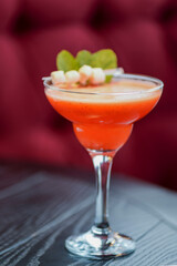 Cold summer alcohol cocktail with ice and fruit in a tall glass on light blurred restaurant or cafe background.