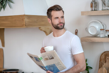 Dark-haired handsome man holding a newspaper aand having coffee