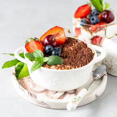 A beautiful portioned serving of Italian tiramisu dessert, garnished with strawberries, cherries and mint on a white background. Square