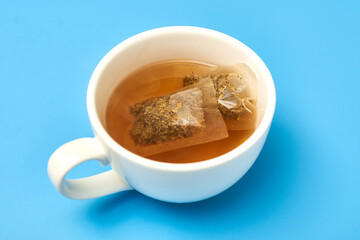 Tea bag in a white cup on a blue background. Making delicious herbal tea.