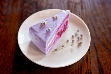 Slice of purple lavender cake with berries served with lavender flowers on a white plate.