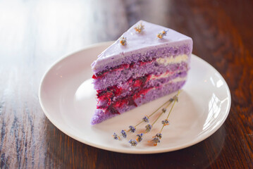 Slice of purple lavender cake with berries served with lavender flowers on a white plate.