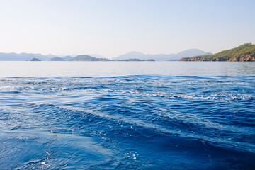 Peaceful seascape. Beautiful blue sky over calm sea with sunlight reflection. Sea waves. Mountains on horizon.