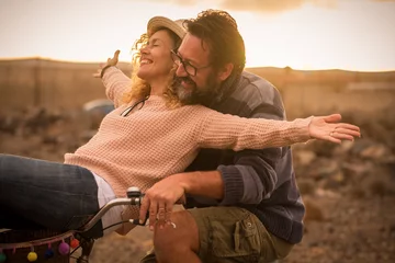Fotobehang Happy adult people cheerful couple enjoy the outdoor leisure activity riding a bike together man carrying woman and laugh a lot in friendship and relationship - active youthful persons © simona