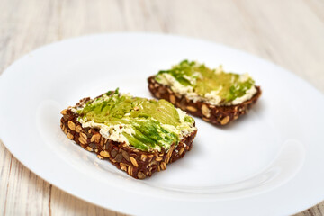 Slice of cereal bread with cream cheese and avocado on a white plate. Vegetarian sandwich.