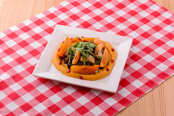 Minced meat with mashed fruit puree on white plate over red plaid tablecloth background.