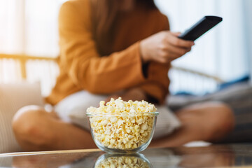 Close up image of a woman eating pop corn and searching channel with remote control to watch tv while sitting on sofa at home