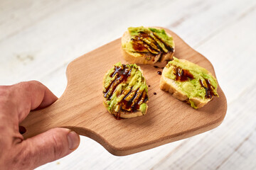 Baguette, bruschetta, canapes with avocado and maple syrup on a light wooden background.