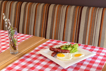 Breakfast with salad, fried egg and sausages served in white plate over red plate tablecloth.