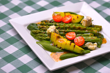 Healthy grilled avocado and asparagus salad with linen seeds and tomatoes. Served on a white square plate.