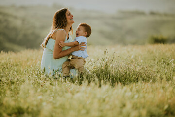 Young pregnant mother with her cute little boy in the field on beautiful sunny day
