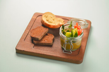 Plate with fresh vegetables and thick sauce in a jar, with different kinds of bread, served on a rustic wooden board.