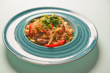 Plate of Asian chicken salad with rice noodles and sesame seeds served in a blue plate over blue mint background.