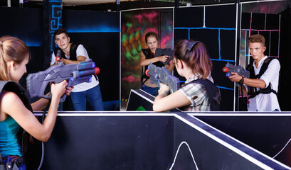 Two laser tag teams playing enthusiastically and aiming at each other in dark room