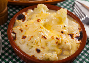 Tasty  baked cauliflower with bechamel sauce in clay pot at table