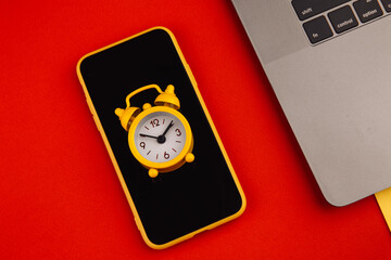 Overtime concept. Laptop, smartphone and clock on red background close up.