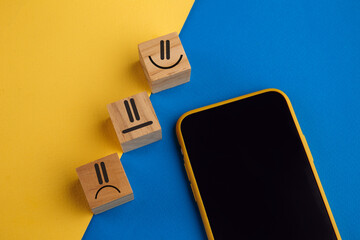 Obraz premium Emotion face symbol on wooden cube blocks and smartphone. Service rating, ranking, customer review, satisfaction and feedback concept.