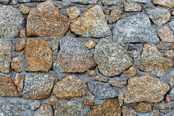 colored unprocessed rocky stones of natural origin, a wall of stones in concrete, background for walls and wallpapers, large stones in focus