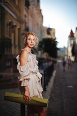 beautiful woman in a fashionable dress holds a carimat for practicing yoga in the city center on a sunset background