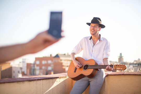 Joven cantante actuando por streaming en redes sociales en la azotea de un edificio al atardecer