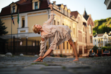 Beautiful blonde woman in nice dress  doing a yoga exercise in city on sunset background