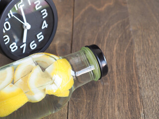 Water and lemons slice in glass bottle with clock on wooden background, drink for detox, and refresh the body..