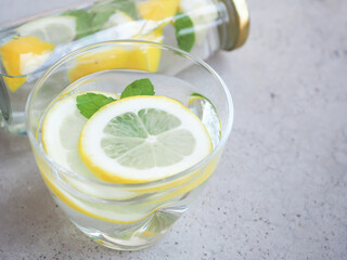 Water and lemons slice in glass with mint leaves and bottle on grey background, drink for detox, and refresh the body..