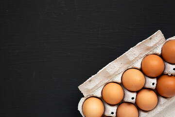 Raw Brown Eggs in a paper box on a black background, top view. Flat lay, overhead, from above. Space for text.