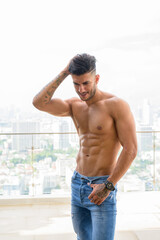 Fototapeta premium Happy young handsome muscular Persian man shirtless against view the city