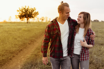 Outdoor shot of young couple walking through meadow hand in hand. Man and woman talking walk through grass field