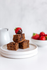 Fresh baked tasty chocolate brownies with strawberry and chocolate sauce on white marble background