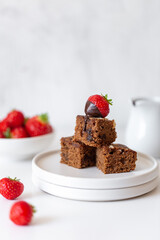 Fresh baked tasty chocolate brownies with strawberry and chocolate sauce on white marble background