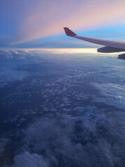 Fototapeta premium Flight from Moscow to Thailand. View from the porthole of an aircraft on clouds, sea and islands. Travel by plane to different countries. Boeing jet. Sunset view from plane. Image with noise effect.