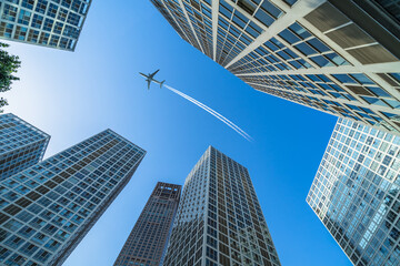 Obraz na płótnie Canvas Tall city buildings and a plane flying overhead