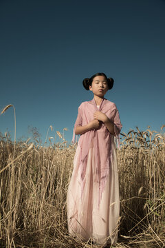 Thoughtful girl in dress standing in wheat field