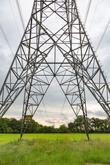 Electricity pylons in a green meadow under a threatening sky.