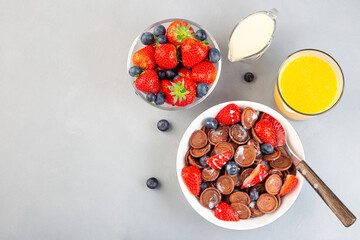 Trendy small chocolate cereal pancakes served with condensed milk, strawberry, blueberry and orange juice, in a white bowl, horizontal, top view, copy space