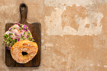 top view of fresh delicious bagel with meat, red onion and sprouts on wooden cutting board on aged...