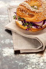 fresh delicious bagel with meat, red onion, cream cheese and sprouts on napkin on textured surface